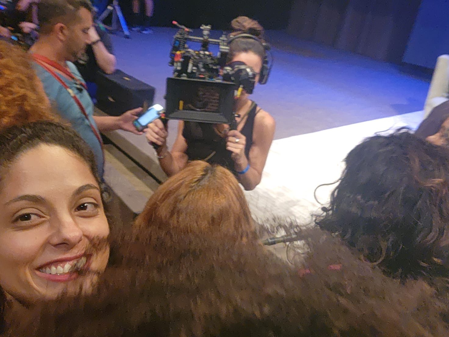 Amanda sorrindo em set de filmagem, com câmera ao fundo